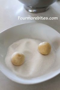 Lemon sugar cookie dough balls sitting in a white bowl with sugar, ready to be rolled.  