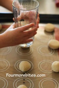 Pressing down the lemon sugar dough balls, on a cookie sheet, with a water glass