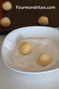 Rolled lime sugar cookie dough balls in white sugar in a white bowl.