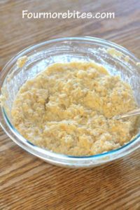 Cheese, rice, chicken broth and seasonings mixed together in a clear glass pyrex bowl on an oak table