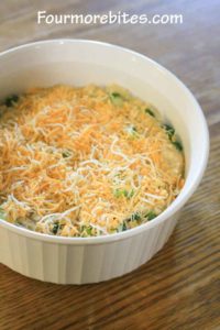 Cheesy rice and broccoli casserole topped with shredded cheese in a white corningware dish sitting on an oak table