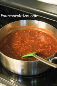 Chili simmering in a stainless steel pot on a black stovetop