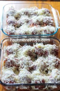 Stuffed pasta shells with marinara, mozzarella cheese and Parmesan cheese layerd on top in two 8x8 glass pans on a wooden table.