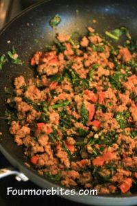 Sausage, ground beef, spinach, tomatoes and onions in a black skillet.